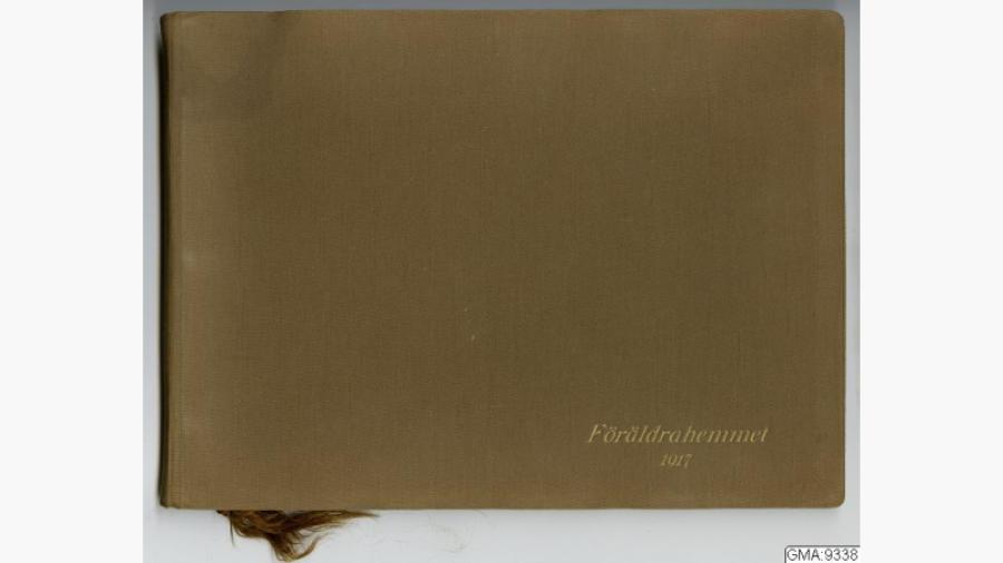 Fotoalbum i brun kartong, bunden med brun snodd. På framsidan guldtryck "Föräldrahemmet 1917". Albumet innehåller 14 svartvita bilder, 1 exteriör och 13 interiörbilder från Emil Haglunds på Storgatan 41. Källa: Databasen Carlotta, Göteborgs stadsmuseum